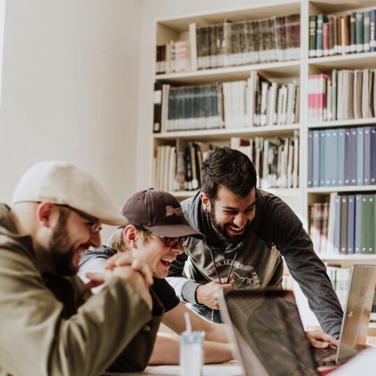 Three men collaborating over a laptop in a cozy library.